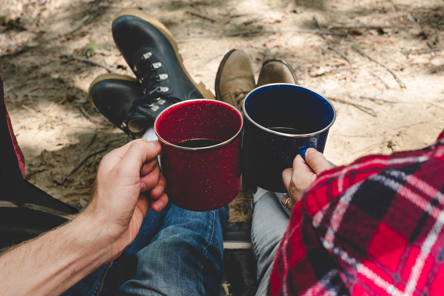 Two camping mugs of coffee held by two people sitting next to each other.